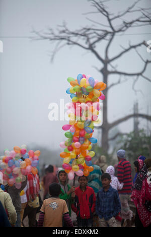 Garçon transporte bangladais des ballons pour vendre pendant qu'il observe les dévots musulmans à pied pour assister à la prière finale de la Congrégation islamique de trois jours sur les rives de la rivière Turag à Tongi, 20 kilomètres (13 milles) au nord de la capitale Dacca. Des centaines de milliers de Musulmans ont participé au congrès annuel de l'événement de trois jours qui est l'un des plus grands rassemblements religieux détenu depuis 1960 pour relancer les principes islamiques. Il dévalorise la politique et appelle à la paix. Banque D'Images