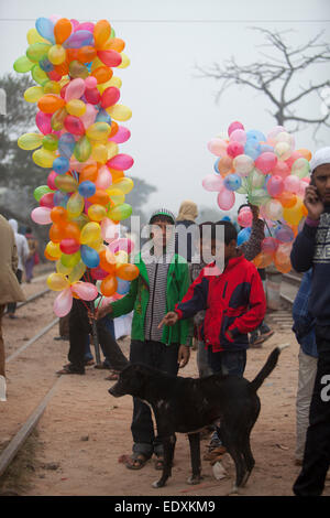 Garçon transporte bangladais des ballons pour vendre pendant qu'il observe les dévots musulmans à pied pour assister à la prière finale de la Congrégation islamique de trois jours sur les rives de la rivière Turag à Tongi, 20 kilomètres (13 milles) au nord de la capitale Dacca. Des centaines de milliers de Musulmans ont participé au congrès annuel de l'événement de trois jours qui est l'un des plus grands rassemblements religieux détenu depuis 1960 pour relancer les principes islamiques. Il dévalorise la politique et appelle à la paix. Banque D'Images