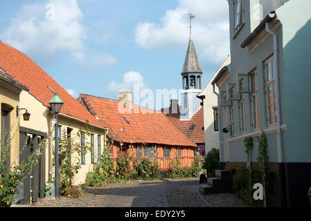 Une longue pierre pavée bordée de cottages traditionnels danois sur Overgade à Ebeltoft, Danemark La tour de l'horloge est Ebeltof Banque D'Images