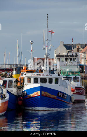 Les petits bateaux de pêche colorés ou de navires, sont amarrés côte à côte dans l'eau de sunny, scenic Whitby Harbour - Côte du Yorkshire du Nord, Angleterre, Royaume-Uni. Banque D'Images