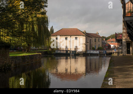 Bâtiment historique rénové bâtiment de l'entrepôt et 2 bateaux amarrés, reflétée dans l'eau calme du bassin du canal - Canal de Ripon, North Yorkshire, Angleterre, Royaume-Uni. Banque D'Images