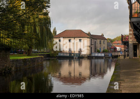 Bâtiment historique rénové bâtiment de l'entrepôt et 2 bateaux amarrés, reflétée dans l'eau calme du bassin du canal - Canal de Ripon, North Yorkshire, Angleterre, Royaume-Uni. Banque D'Images