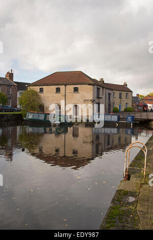 Bâtiment historique rénové bâtiment de l'entrepôt et 2 bateaux amarrés, reflétée dans l'eau calme du bassin du canal - Canal de Ripon, North Yorkshire, Angleterre, Royaume-Uni. Banque D'Images