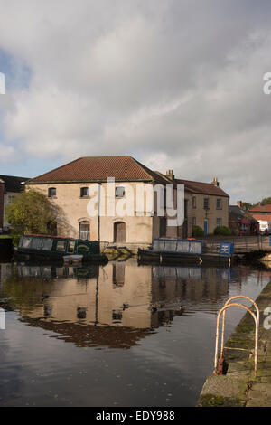 Bâtiment historique rénové bâtiment de l'entrepôt et 2 bateaux amarrés, reflétée dans l'eau calme du bassin du canal - Canal de Ripon, North Yorkshire, Angleterre, Royaume-Uni. Banque D'Images