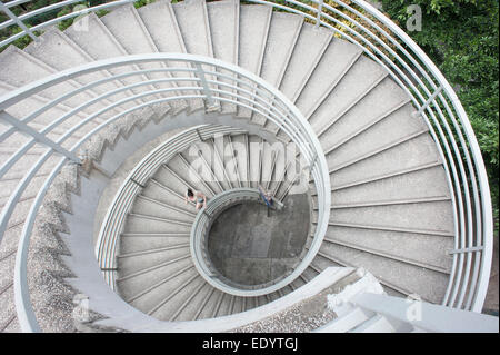 Vue abstraite au-dessus regardant droit dans un escalier en colimaçon blanc à Hong Kong, avec une figure solitaire ascendante loin en dessous, composition géométrique. Banque D'Images