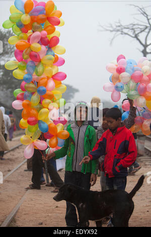 Garçon transporte bangladais des ballons pour vendre pendant qu'il observe les dévots musulmans à pied pour assister à la prière finale de la Congrégation islamique de trois jours sur les rives de la rivière Turag à Tongi, 20 kilomètres (13 milles) au nord de la capitale Dacca. Des centaines de milliers de Musulmans ont participé au congrès annuel de l'événement de trois jours qui est l'un des plus grands rassemblements religieux détenu depuis 1960 pour relancer les principes islamiques. Il dévalorise la politique et appelle à la paix. Banque D'Images