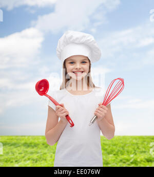 Smiling girl in cook hat avec louche et fouetter Banque D'Images