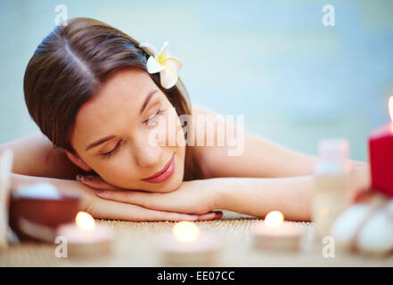 Femme détendue avec fleur de frangipanier dans les cheveux se reposant dans spa salon Banque D'Images