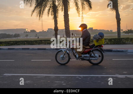 Un travailleur migrant chefs pour travailler sur une moto à Doha, au Qatar, au lever du soleil Banque D'Images
