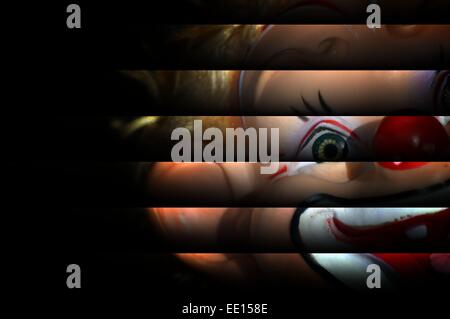 Scary clown doll apparaissant être peering through blinds. clown sur fond sombre,la moitié des yeux visage clown Banque D'Images