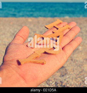 La main d'un jeune homme montrant des lettres formant le mot heureux, sur la plage, avec un effet de filtre Banque D'Images