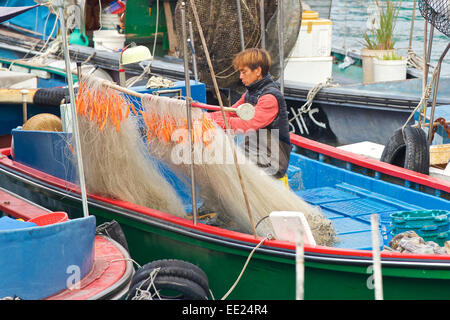 Jeune pêcheur chinois raccommodage des filets dans un petit bateau de pêche sur l'île de Cheung Chau, Hong Kong. Banque D'Images