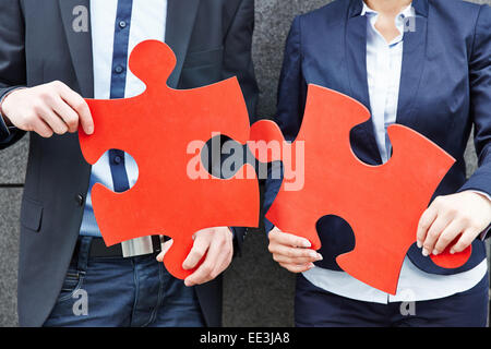 Deux personnes tenant deux big red jigsaw puzzle pieces Banque D'Images