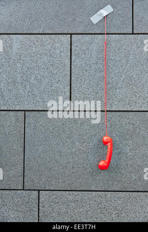 Téléphone rouge pendant vers le bas avec du ruban adhésif sur un mur gris Banque D'Images