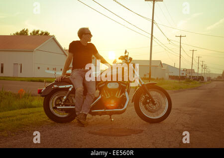 Les jeunes hommes avec sa moto Harley Davidson à la voiture en face d'un merveilleux coucher du soleil en été Banque D'Images