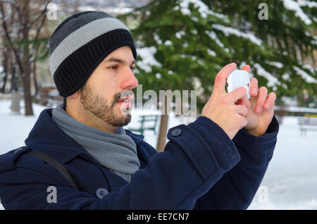 Jeune homme en prenant une photo avec son smartphone en hiver Banque D'Images