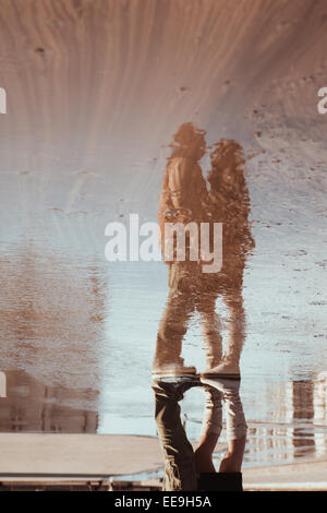 Reflet dans flaque de femme et l'homme embrassant sous la pluie au cours de parapluie Banque D'Images