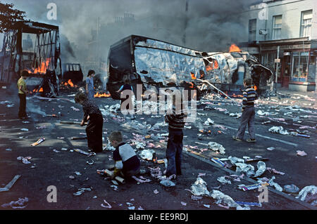 BELFAST, Royaume-uni - août 1976 ; enfants jouant parmi les débris des véhicules qui brûlent détourné après des émeutes dans l'Ouest de Belfast durant les troubles, l'Irlande du Nord. Banque D'Images