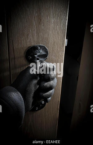 La main gantée de l'ouverture d'une porte dans une pièce sombre. Banque D'Images