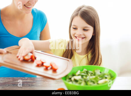 Petite fille avec la mère d'ajouter à la salade de tomates Banque D'Images