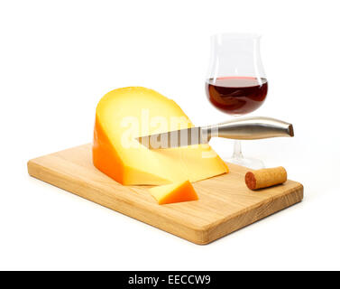 La vie encore d'un couteau à fromage jaune sur une planche à découper avec un verre de vin rouge contre fond blanc Banque D'Images