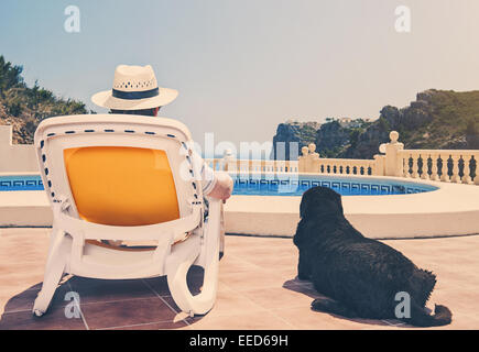 Propriétaire de détente au bord de piscine avec chien à côté de lui Banque D'Images