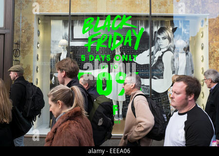 Shoppers sur Oxford Street au centre de Londres avec un signe noir publicité vendredi dans une vitrine. Banque D'Images