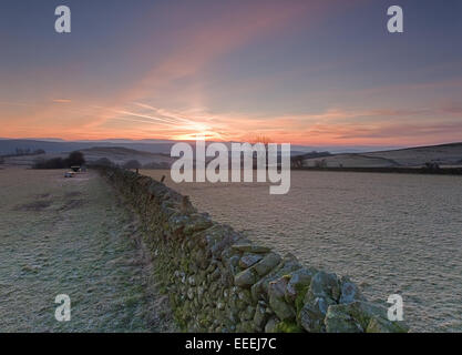 Champs couverts de givre et mur de pierres sèches sur les collines lointaines et les montagnes au lever du soleil Banque D'Images