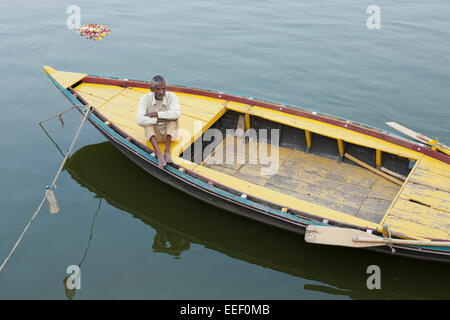 Varanasi, Inde. Bateau à rames sur le Gange. Les clients attendent, batelier fleurs votive en flottant Banque D'Images