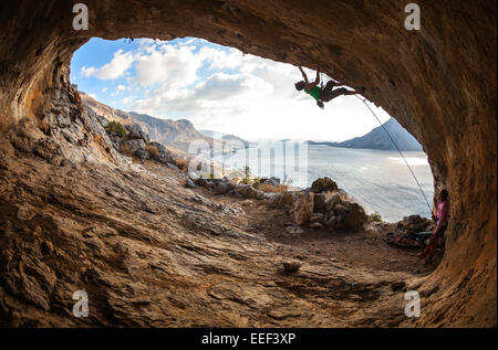 Male rock climber grimpant le long d'un toit dans une grotte Banque D'Images