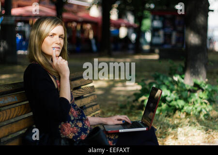 Les jeunes femmes professionnelles contemplatif sur un banc, travailler sur un ordinateur portable à Berlin Banque D'Images