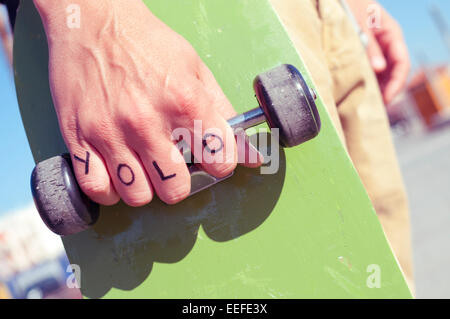 Libre d'un jeune homme avec le mot yolo, on ne vit qu'une fois, tatoué dans sa main est titulaire d'un skateboard Banque D'Images