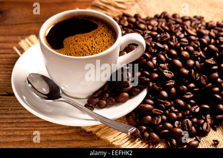 Café fraîchement préparé dans une tasse blanche entourée de grains de café sur une table en bois Banque D'Images