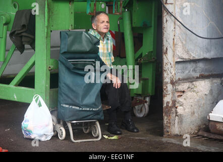 Un homme âgé assis avec panier et sac derrière le marché de la Boqueria à Barcelone Banque D'Images