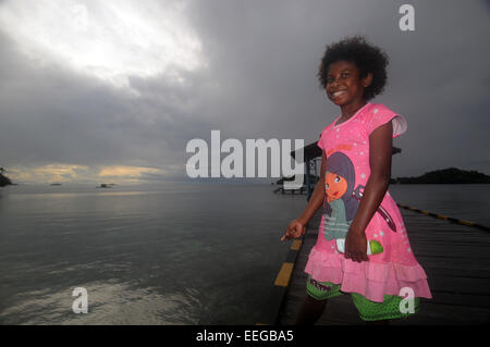 La pêche de la fille son petit-déjeuner au large de la jetée par une matinée pluvieuse, Yenseber village, GAM, l'île de Raja Ampat, province de Papua, Indon Banque D'Images