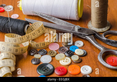Une collection d'outils et fournitures de couture dans un kit de couture, sur table woodem. Articles incluent les fils, boutons, aiguilles, ruban de mesure Banque D'Images
