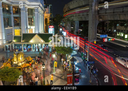 Les fidèles au sanctuaire d'Erawan et centre commercial de luxe entre rue animée de Bangkok, Thaïlande la nuit. Banque D'Images