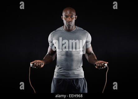 L'homme masculin la corde à sauter dans le noir. Portrait of muscular young man exercising with jumping rope sur fond noir Banque D'Images