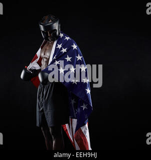 Portrait of african american boxeur avec le drapeau américain drapée autour de son corps contre le fond noir Banque D'Images