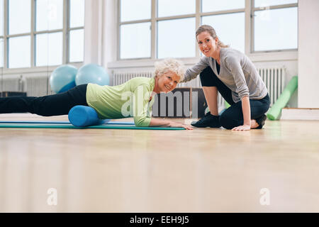 Femme senior exerçant sur un rouleau en mousse avec un entraîneur personnel au gymnase. entraîneur de gymnastique aidant une femme âgée dans son entraînement à heal Banque D'Images