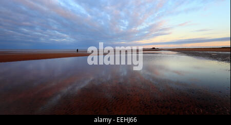 Femme et son chien à la maison au crépuscule sur la plage de Brancaster dans North Norfolk. Banque D'Images