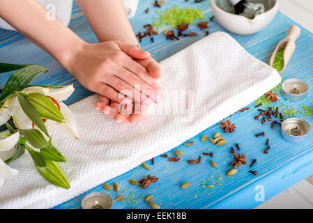 Femme prendre soin de ses mains sur la serviette de bain avec des fleurs, des bougies et des herbes sur un bureau en bois bleu Banque D'Images