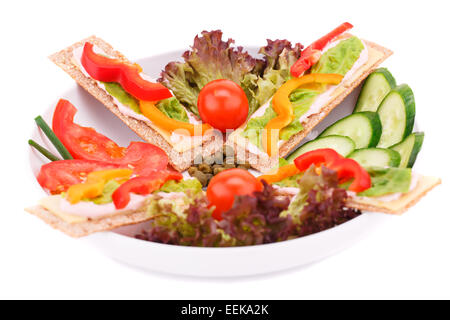 Les crackers avec des légumes frais et du fromage dans la plaque ronde isolé sur fond blanc. Banque D'Images