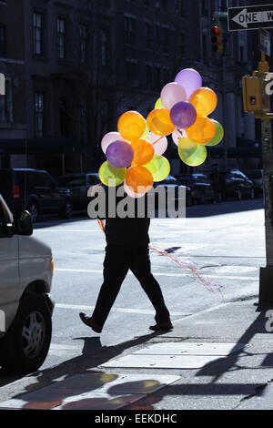 Man crossing 5e Avenue New York street avec un grand groupe de ballons colorés Banque D'Images