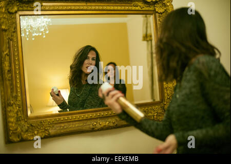 Femme se préparer pour une nuit dehors à la recherche d'elle-même dans un grand miroir doré de pulvériser les cheveux avec une grosse boîte de laque Banque D'Images