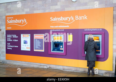 Lady woman using ATM distributeur au supermarché Sainsbury's à Matlock, Derbyshire, Angleterre Banque D'Images