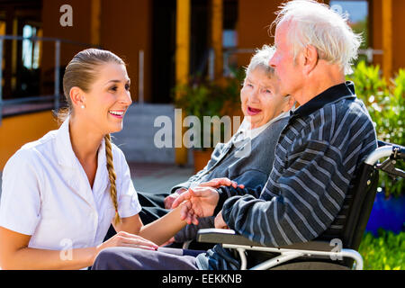 Les personnes âgées, en couple de l'homme et de la femme assise en fauteuil roulant, nurse holding hands avec eux Banque D'Images