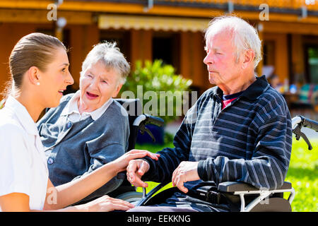 Les personnes âgées, en couple de l'homme et de la femme assise en fauteuil roulant, nurse holding hands avec eux Banque D'Images