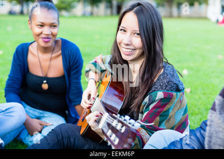 Les amis en chantant des chansons en parc s'amuser ensemble avec une fille à la guitare, au groupe la diversité des pays d'Afrique, d'Asie et du Caucase doivent rejoindre Banque D'Images