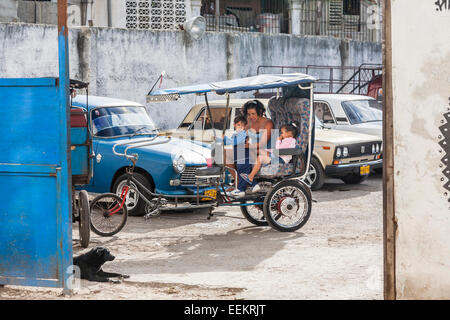 Vie locale : mère cubaine à assister à ses enfants dans un cycle rickshaw taxi dans le quartier de Chinatown, La Havane, capitale de Cuba Banque D'Images